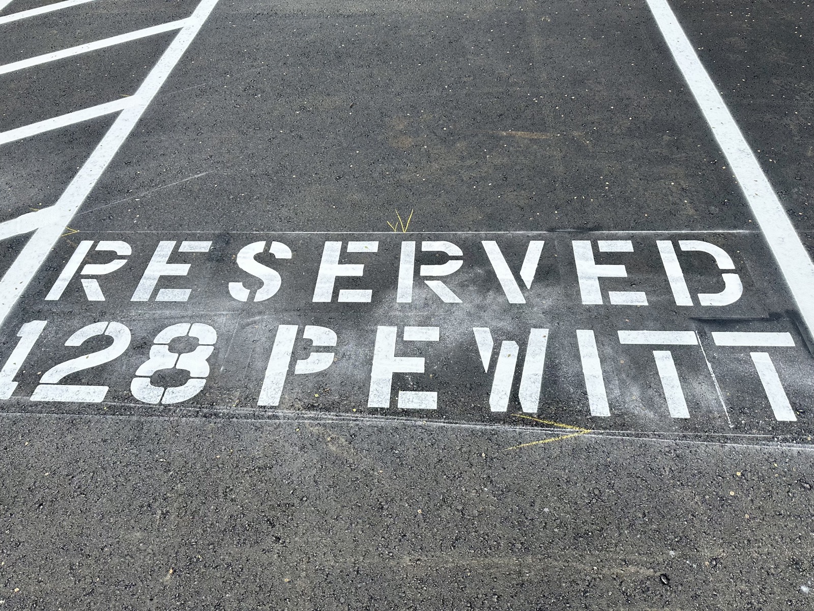 A custom pavement stencil reading RESERVED 128 PEWITT painted in a marked stall